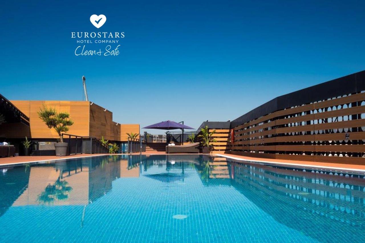 Eurostars Palace Κόρδοβα Εξωτερικό φωτογραφία The photo shows an outdoor swimming pool with clear, blue water, reflecting the blue sky above. The pool area is surrounded by modern architectural features, including wooden slats and potted plants. There is also a purple umbrella providing shade. T