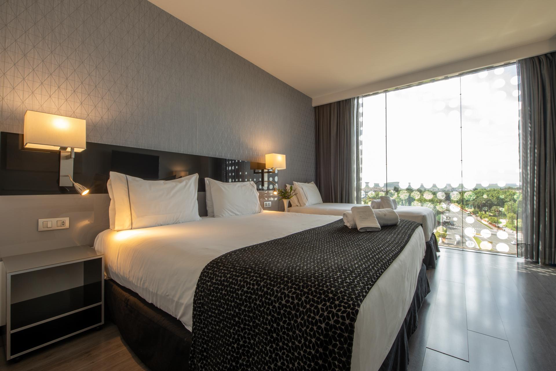 Eurostars Palace Κόρδοβα Εξωτερικό φωτογραφία The photo shows a modern hotel room featuring two large beds with white linens and dark patterned bedspreads. Each bed has a set of pillows and a decorative cushion. There are bedside lamps on either side of the beds, and a contemporary piece of furn