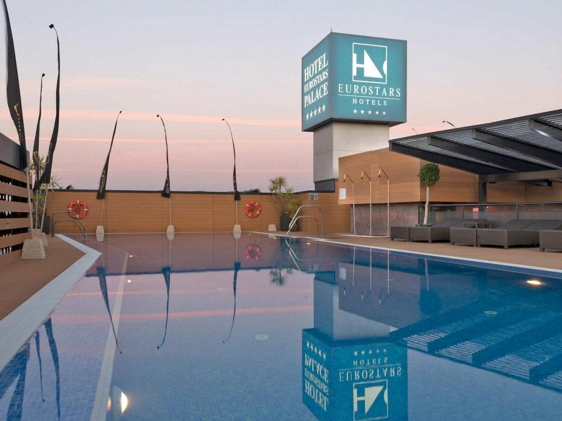 Eurostars Palace Κόρδοβα Εξωτερικό φωτογραφία The image shows a hotel pool area at twilight. The pool is large and reflective, capturing the colors of the sky and surrounding features. In the background, there is a hotel sign displaying the Eurostars brand, with a modern architecture style. The 