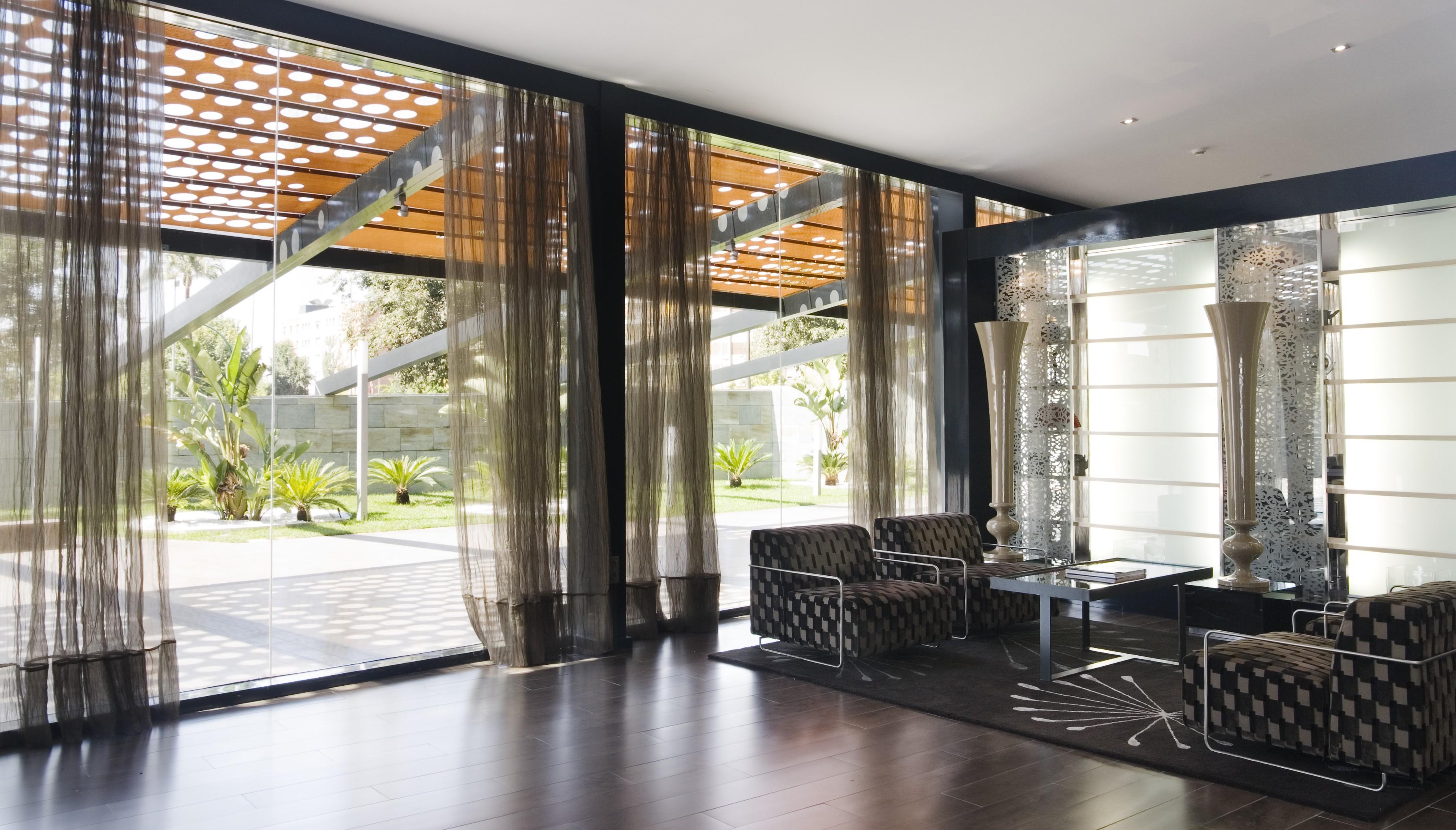 Eurostars Palace Κόρδοβα Εξωτερικό φωτογραφία The photo shows a modern interior space characterized by large windows that allow natural light to flood in. The floor is made of dark wood, which contrasts with the lighter tones of the furnishings. 

In the foreground, there are two stylish chairs 