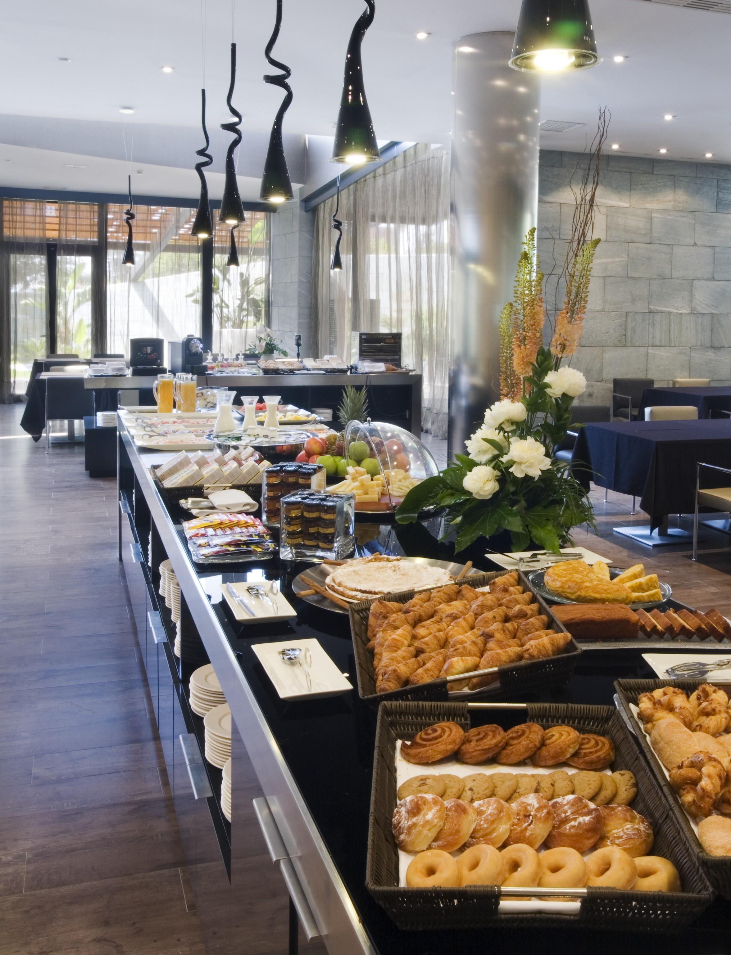 Eurostars Palace Κόρδοβα Εξωτερικό φωτογραφία The photo shows a beautifully arranged buffet spread in a modern setting. There are various dishes displayed on a long table, including pastries, desserts, fruits, and baked goods. A decorative arrangement of flowers enhances the presentation. The ba