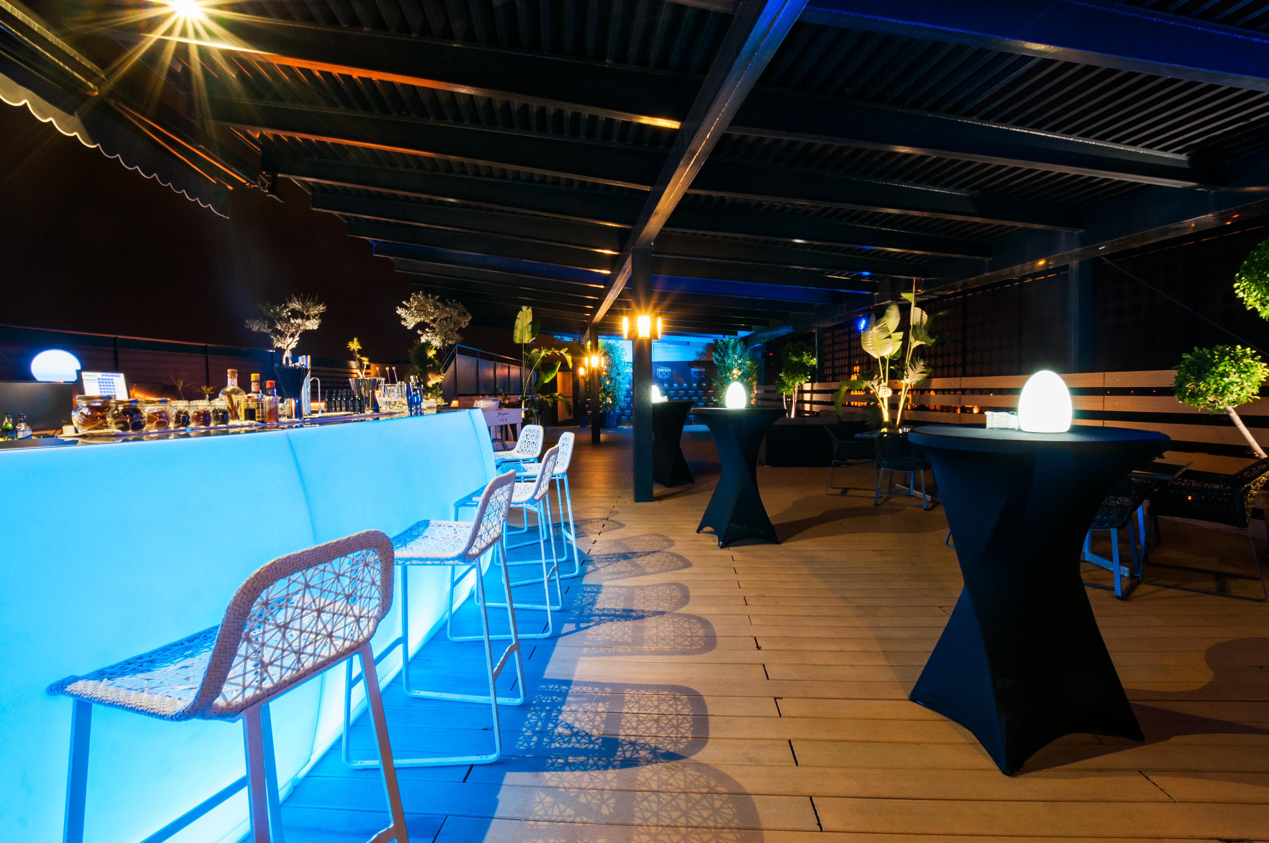 Eurostars Palace Κόρδοβα Εξωτερικό φωτογραφία The photo shows a stylish rooftop or outdoor bar area. There is a long bar counter illuminated with blue lighting, complemented by modern bar stools. The space is decorated with potted plants and elegant round tables covered in black cloth. Soft ligh