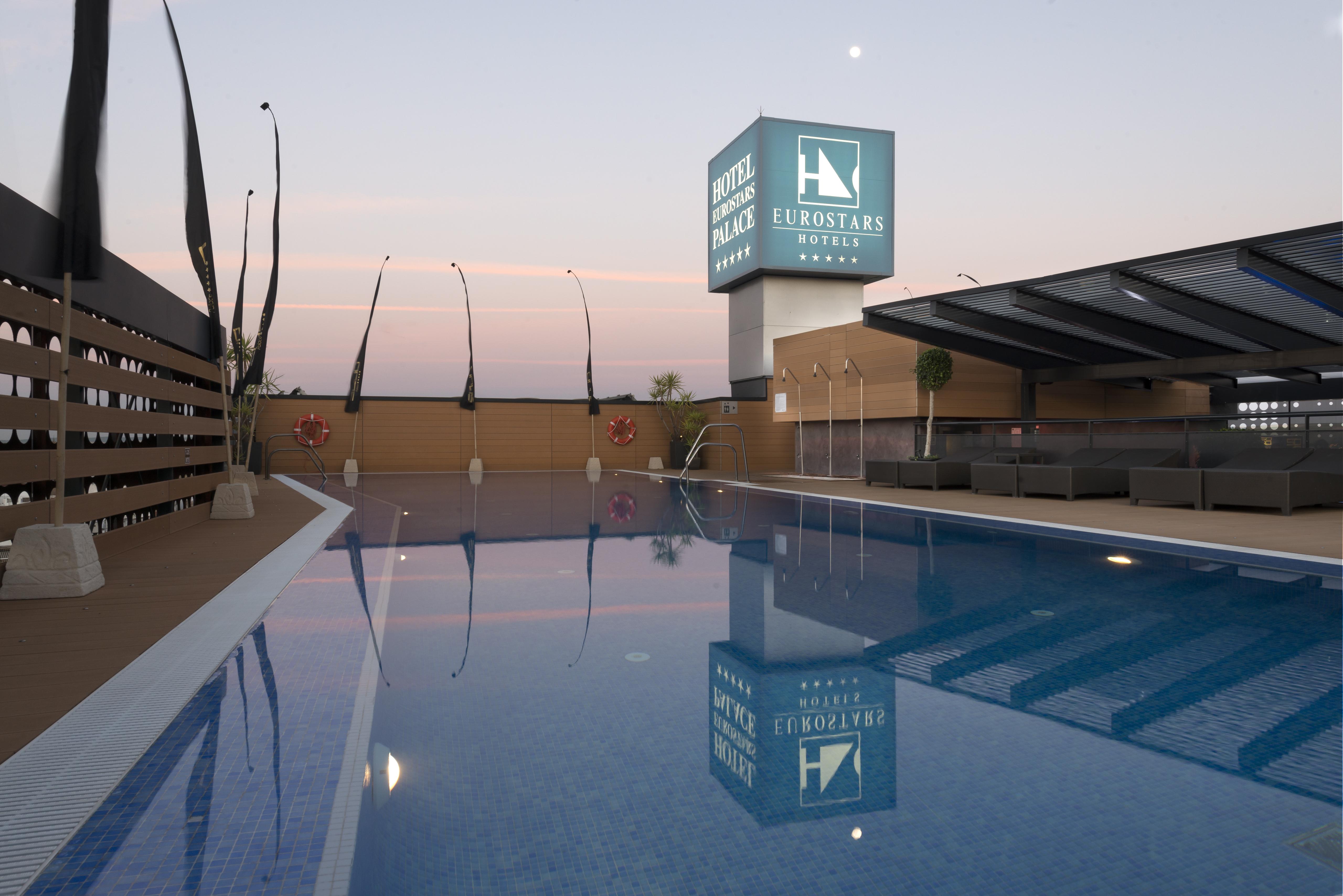 Eurostars Palace Κόρδοβα Εξωτερικό φωτογραφία The photo shows a rooftop space featuring a swimming pool. The pool has a clear blue water, and the area around it is designed with modern aesthetics, including a wooden deck and comfortable seating. In the background, there is a prominent sign for "