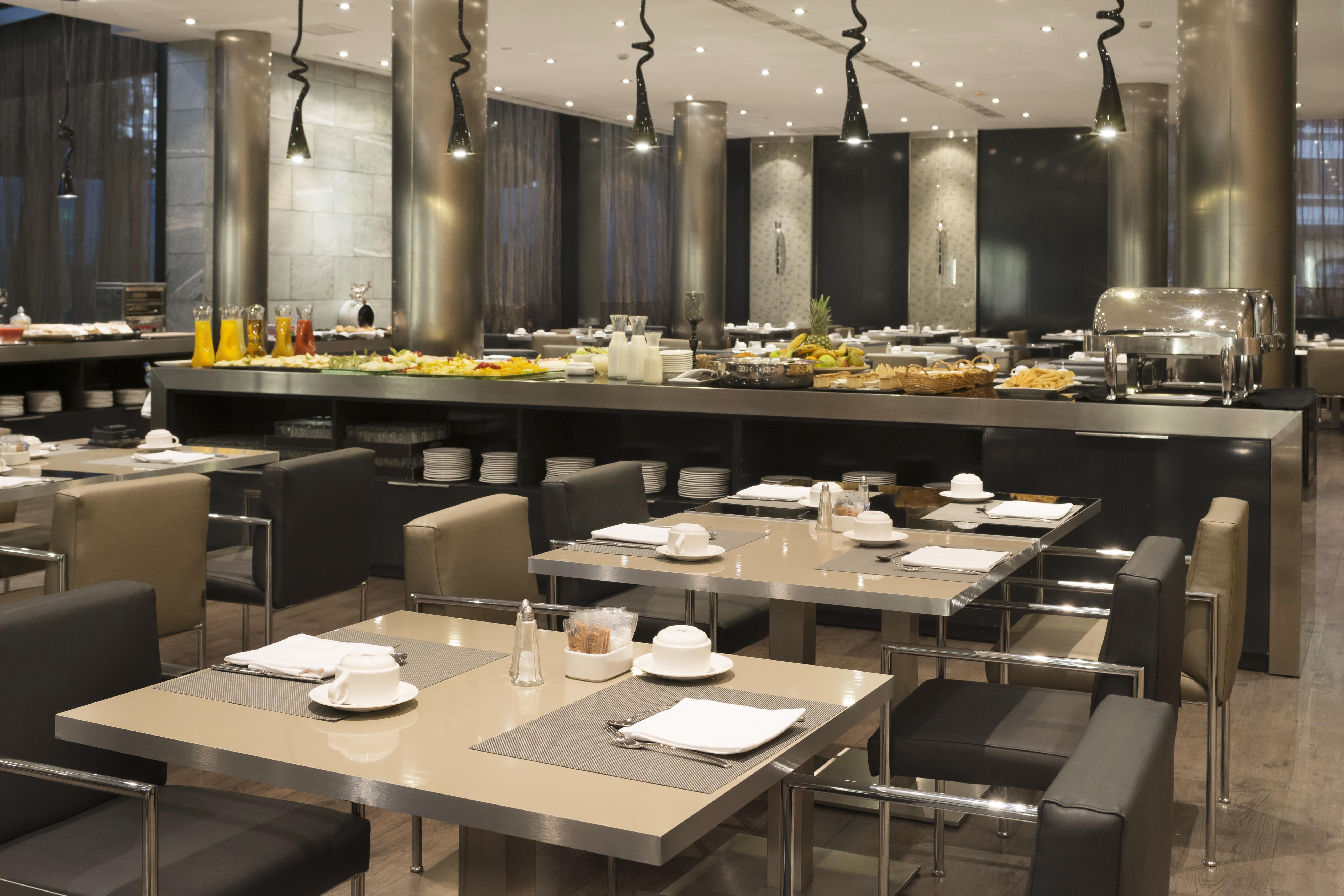 Eurostars Palace Κόρδοβα Εξωτερικό φωτογραφία The photo depicts a modern restaurant interior featuring a spacious dining area with several tables. Each table is set with plates and cutlery, suggesting it's prepared for guests. In the background, there is a buffet station with an extensive displa