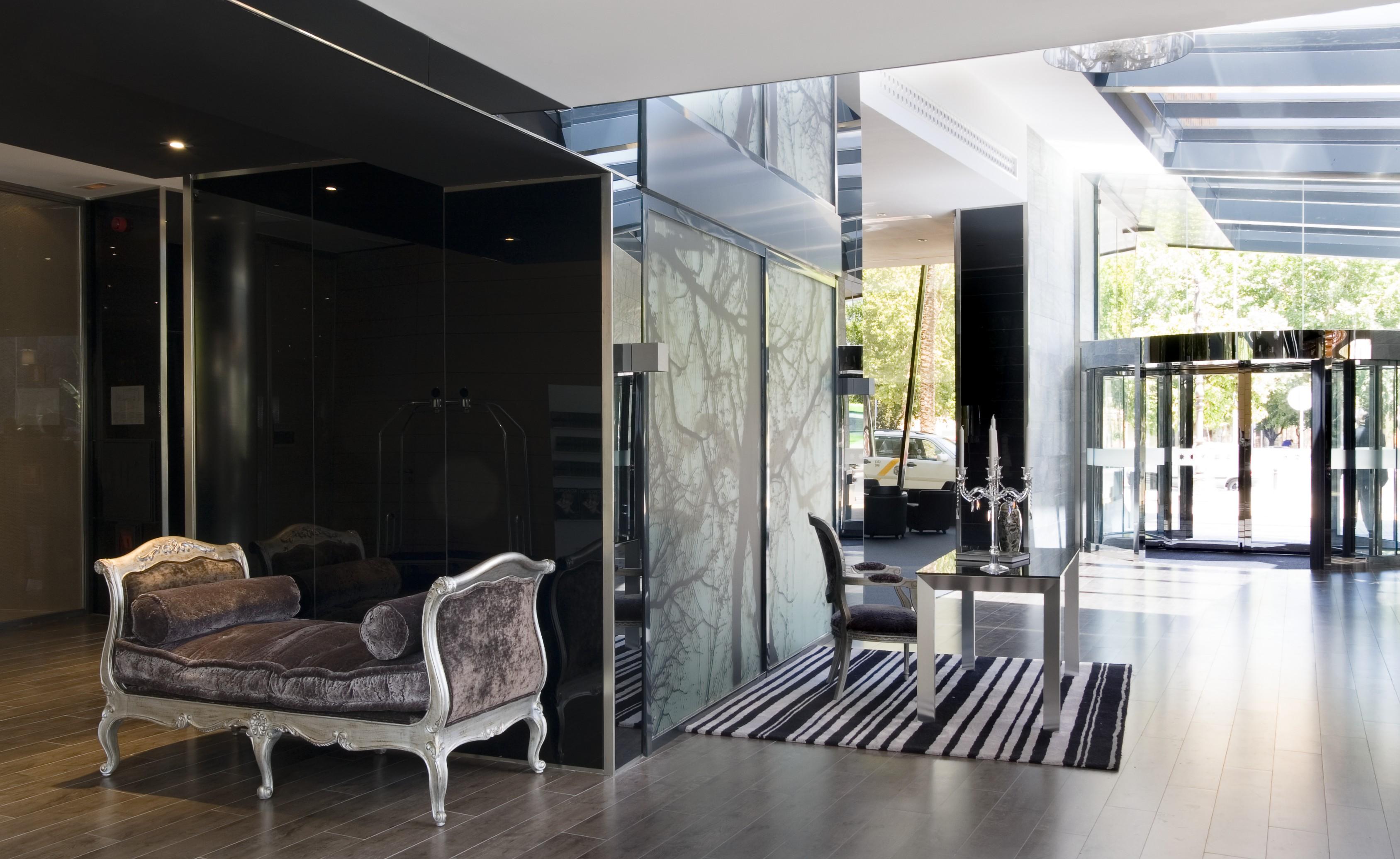 Eurostars Palace Κόρδοβα Εξωτερικό φωτογραφία The photo features a modern and stylish interior space, likely a lobby or reception area. On the left, there is an elegant couch with ornate detailing, set against dark, reflective walls. The floor is wooden and has a sleek design. To the right, ther