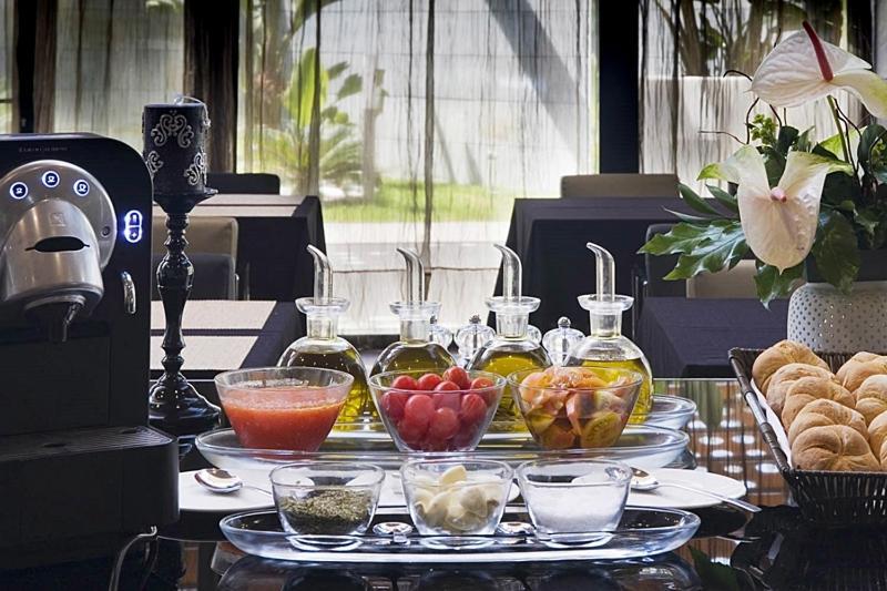 Eurostars Palace Κόρδοβα Εξωτερικό φωτογραφία The photo displays a stylish breakfast or brunch spread on a table. In the foreground, several small glass containers hold various ingredients: there are glasses filled with different types of oil, a bowl of fresh red tomatoes, a bowl of mixed fruit,