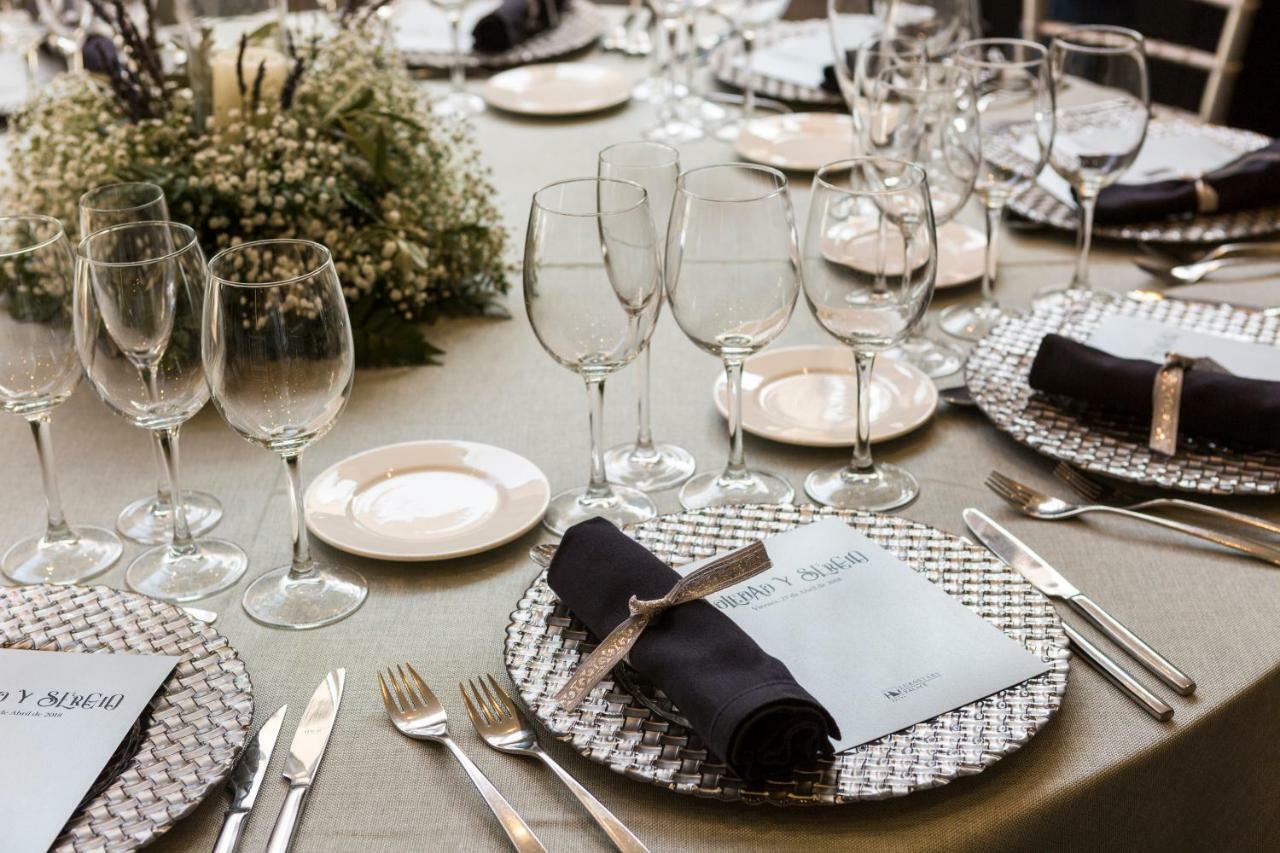 Eurostars Palace Κόρδοβα Εξωτερικό φωτογραφία The photo shows a beautifully arranged dining table set for an event. The table has a neutral-colored tablecloth and is adorned with elegant place settings. Each setting features a decorative plate with a textured silver charger underneath, and a fol
